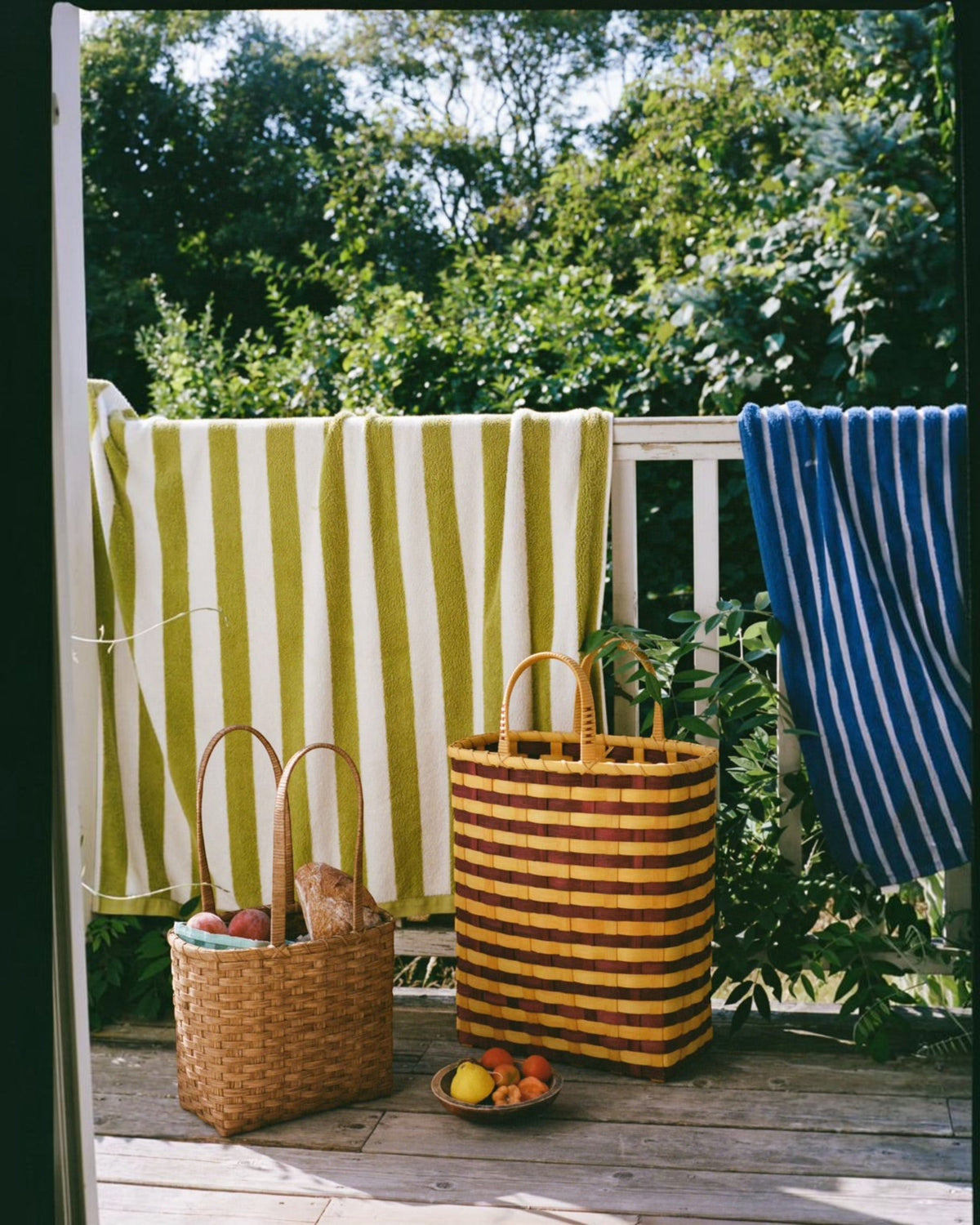 Weldun Carol lunch basket and large woven tote on a sunny wooden deck with striped towels hanging in the background