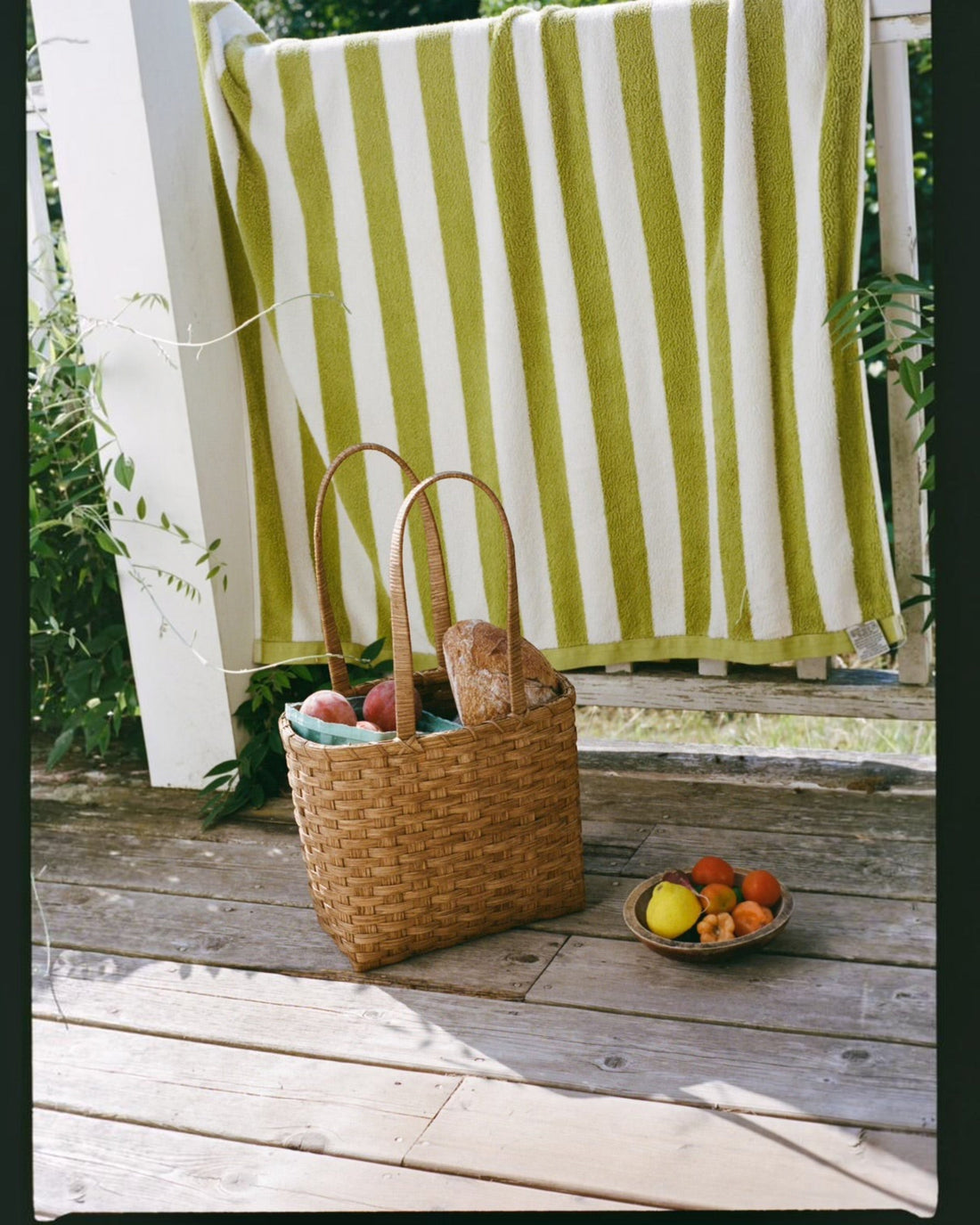 Weldun Carol Lunch Basket hand-woven from natural rattan with a shoulder strap, sitting on a wooden porch.