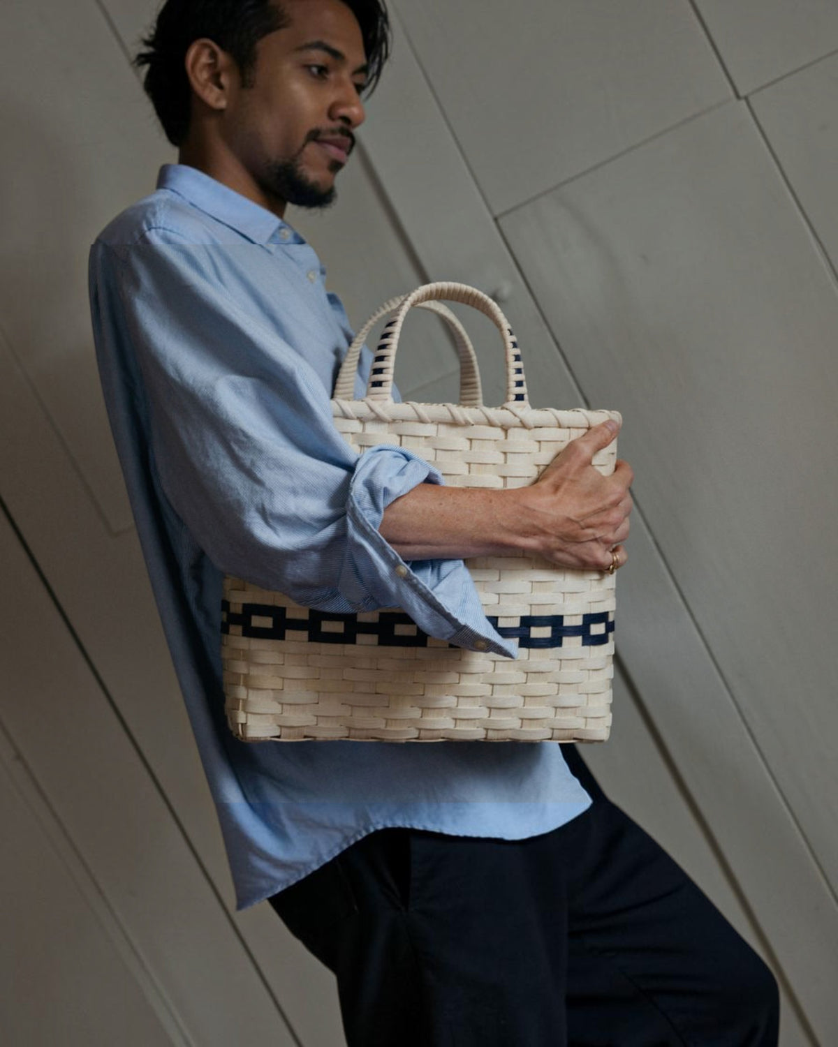 Weldun New England woven rattan shopping basket with navy blue accents held by a man in a light blue shirt.
