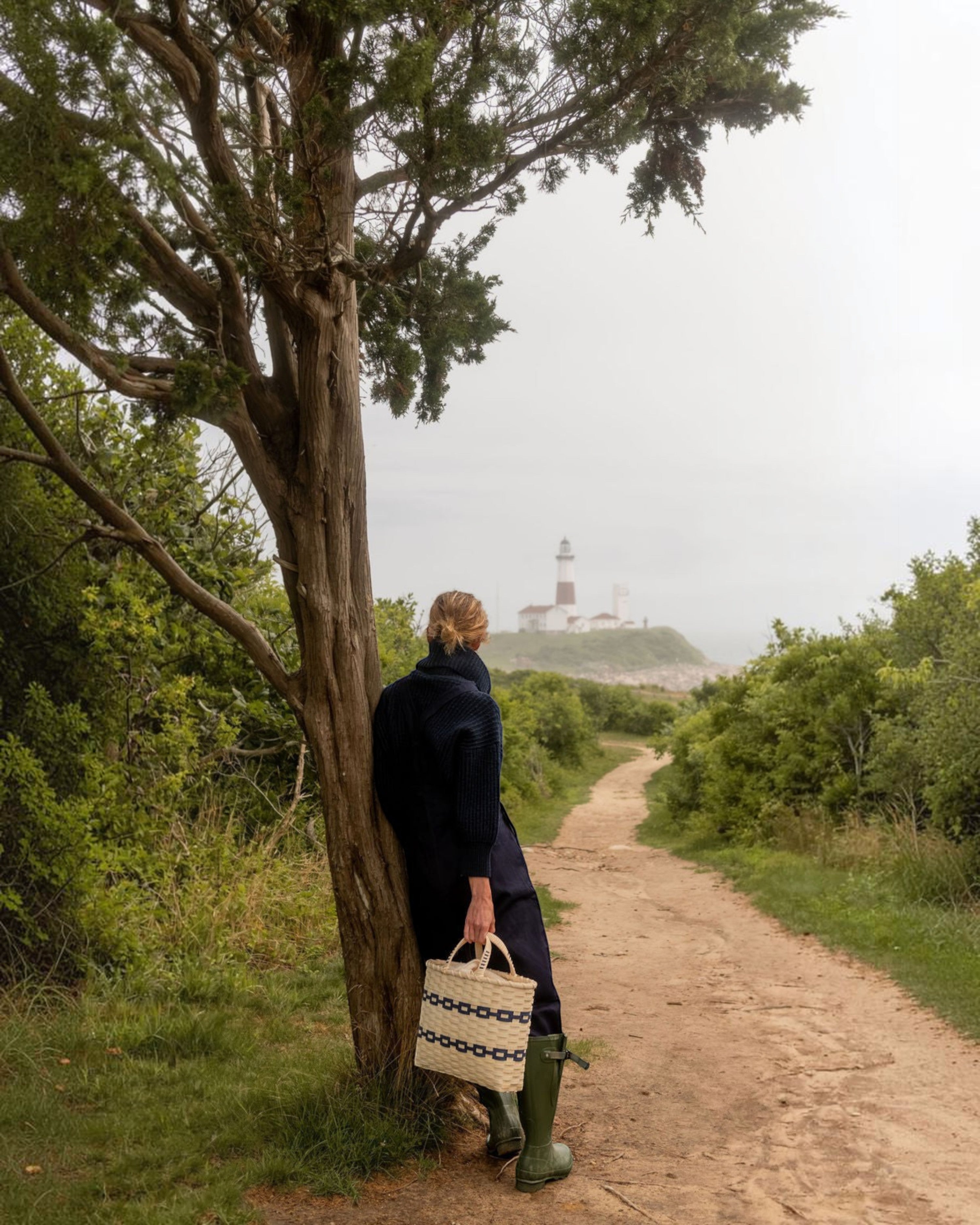 Weldun New England woven rattan shopping basket with blue stripe detail held by a woman on a coastal path