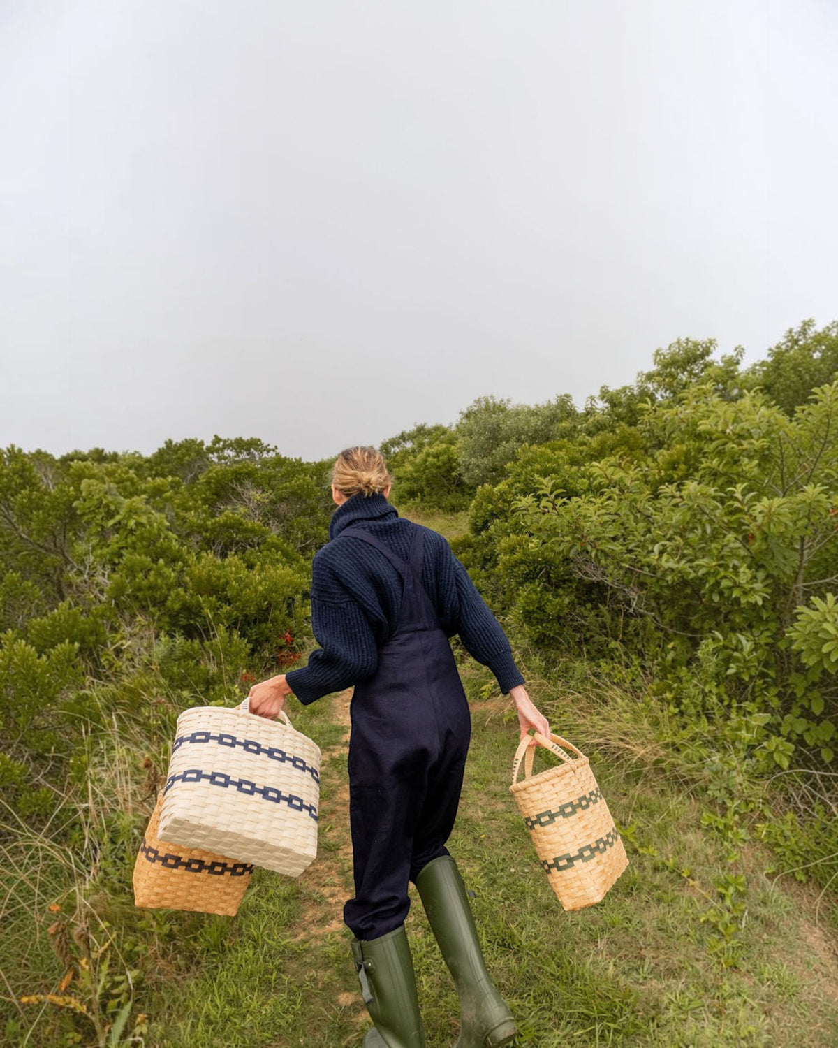Weldun New England woven rattan shopping baskets with blue and green patterns carried by a woman in a coastal field.