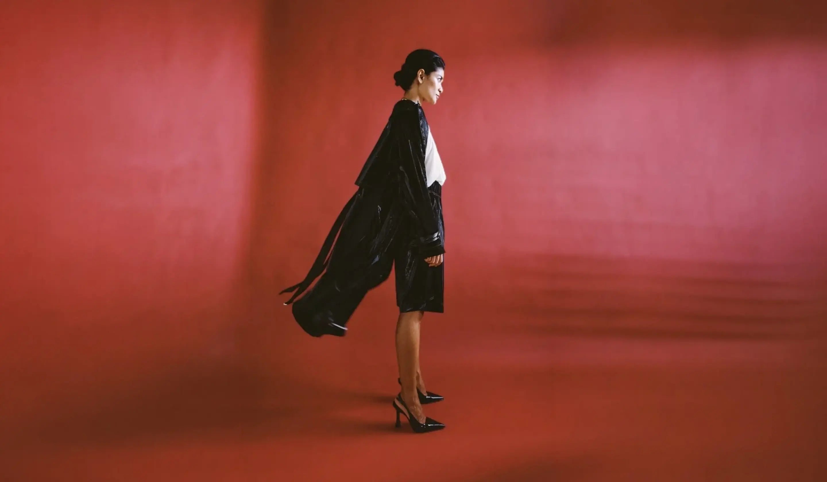 Woman in a black outfit standing against a red background