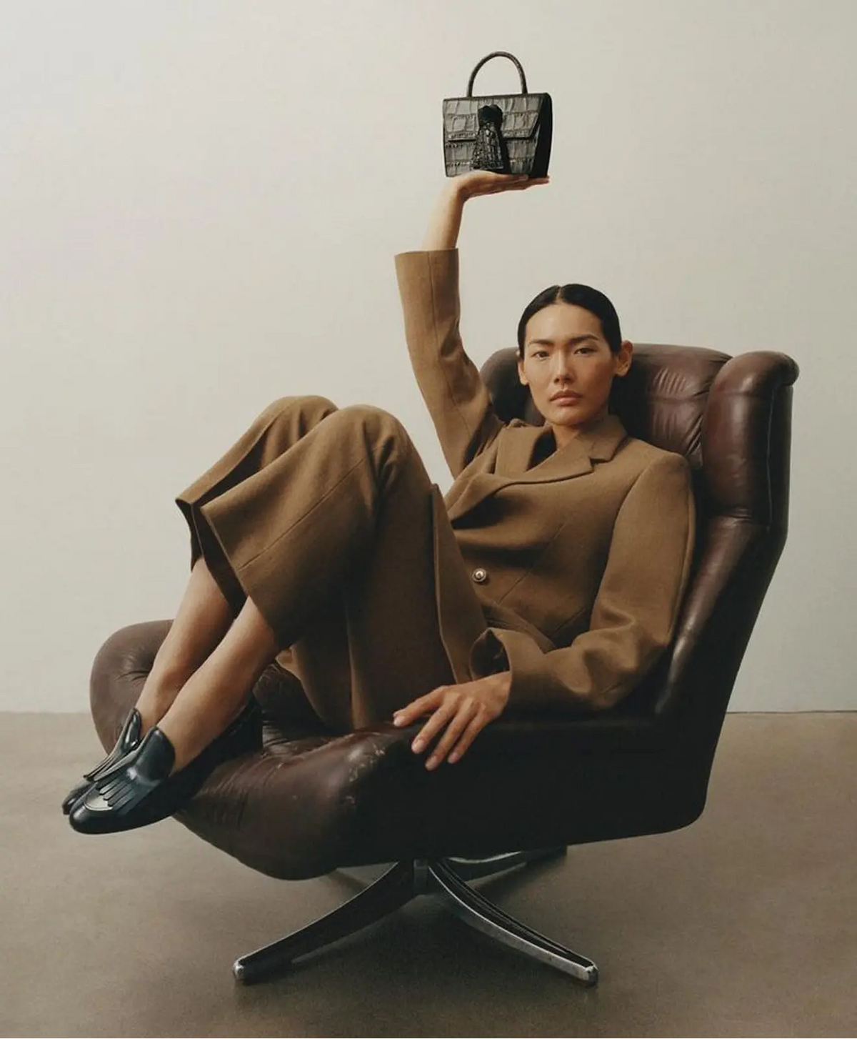 Person in a brown suit sitting in a leather chair holding a handbag.