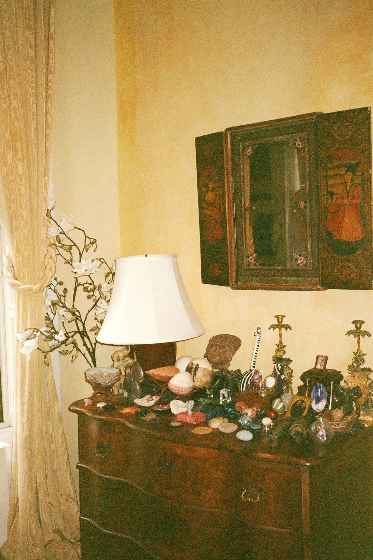 An antique dresser covered with small objects beneath a lamp and a painted cabinet