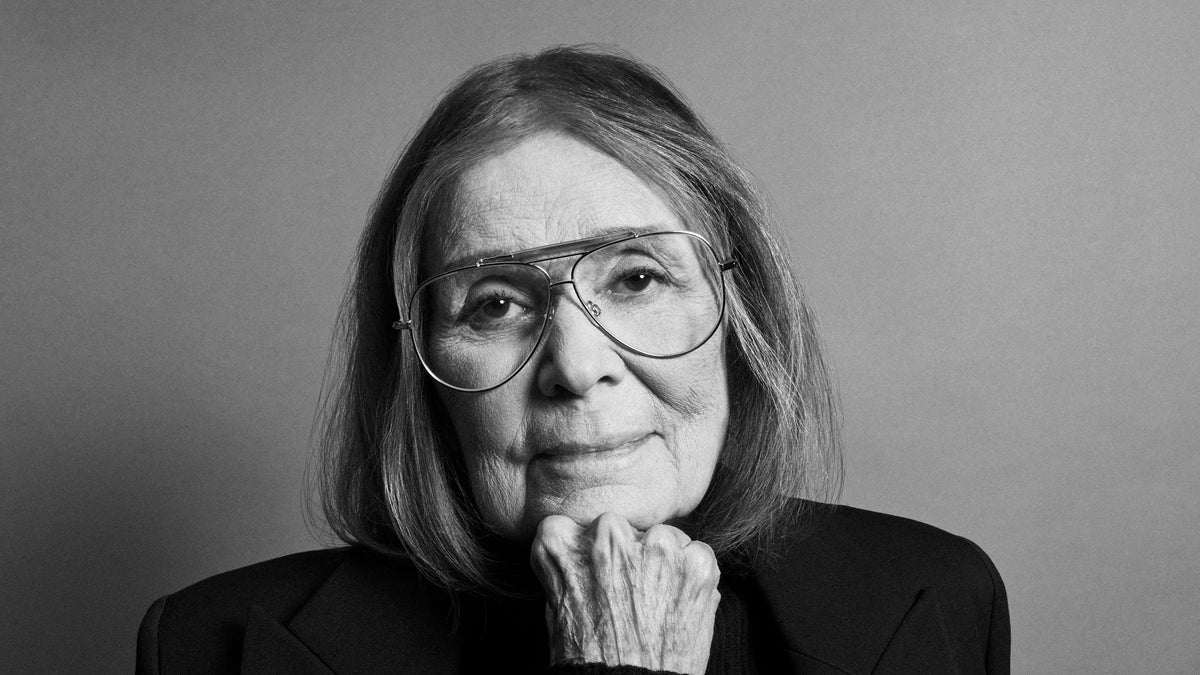 Gloria Steinem in aviator glasses, chin resting on her hand, in black and white