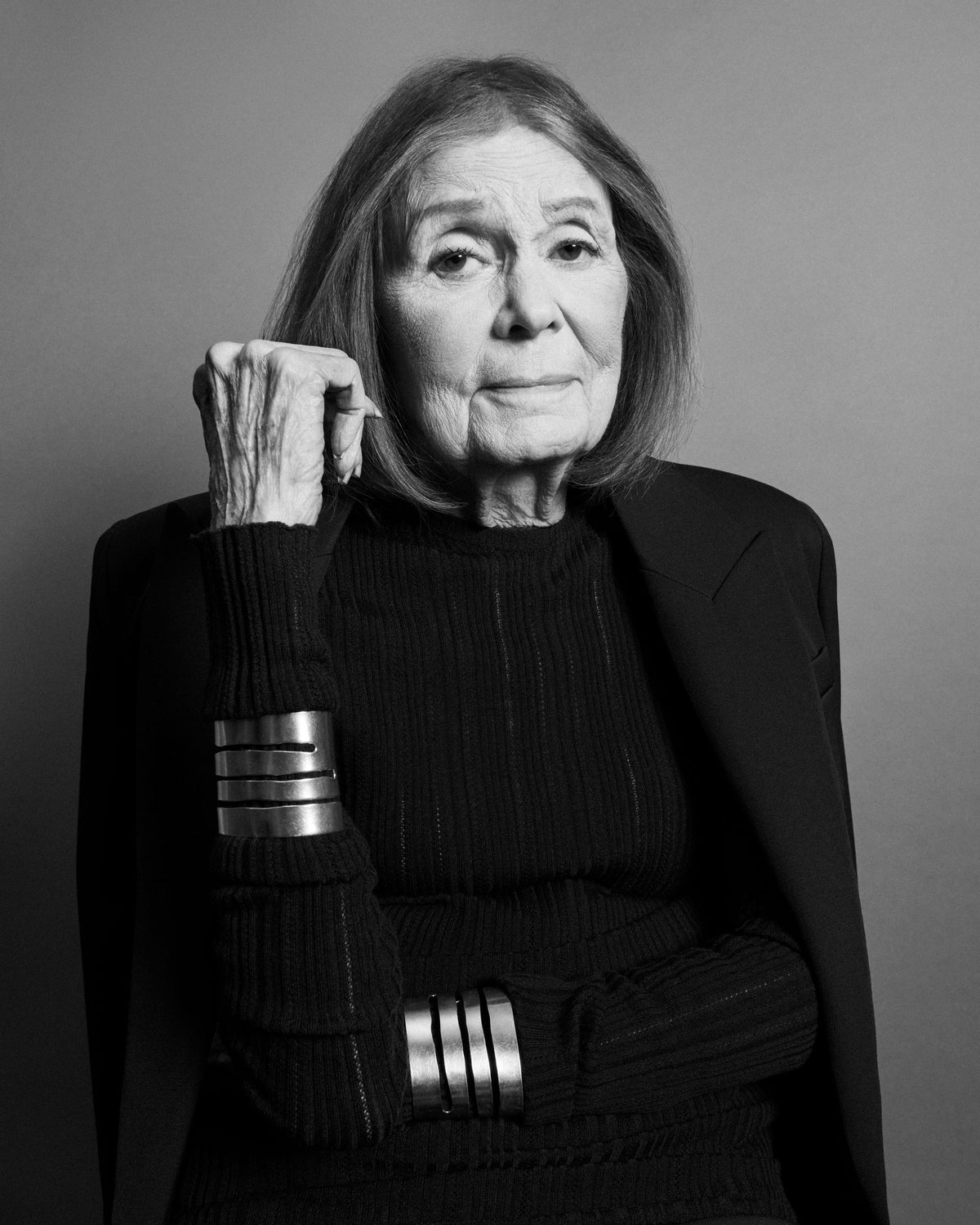 Gloria Steinem in a black jacket and stacked silver cuffs, in black and white