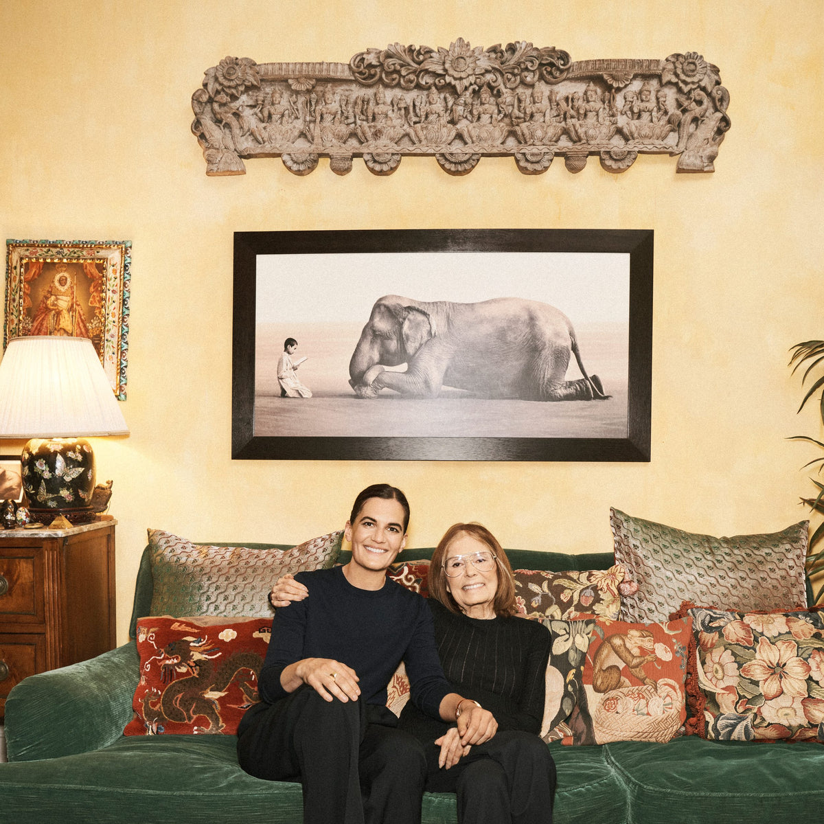 Gloria Steinem and a friend sitting together on a green velvet sofa at home