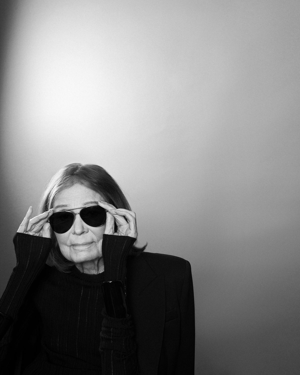 Gloria Steinem adjusting her dark aviator sunglasses, in black and white